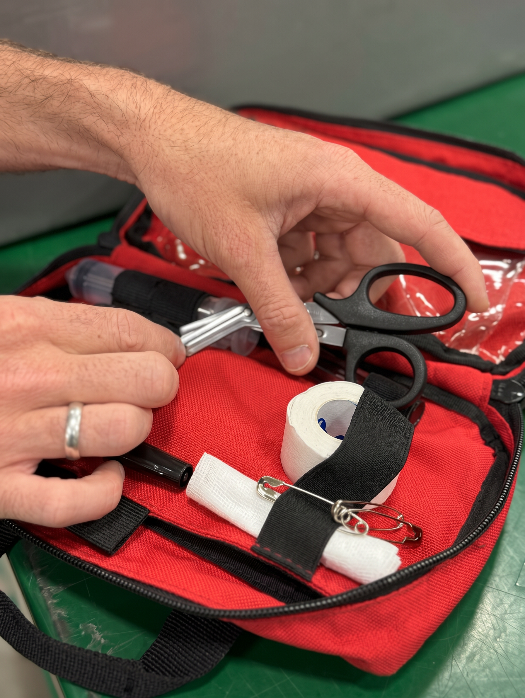 Hands arranging shears and supplies inside an open red medical organizer